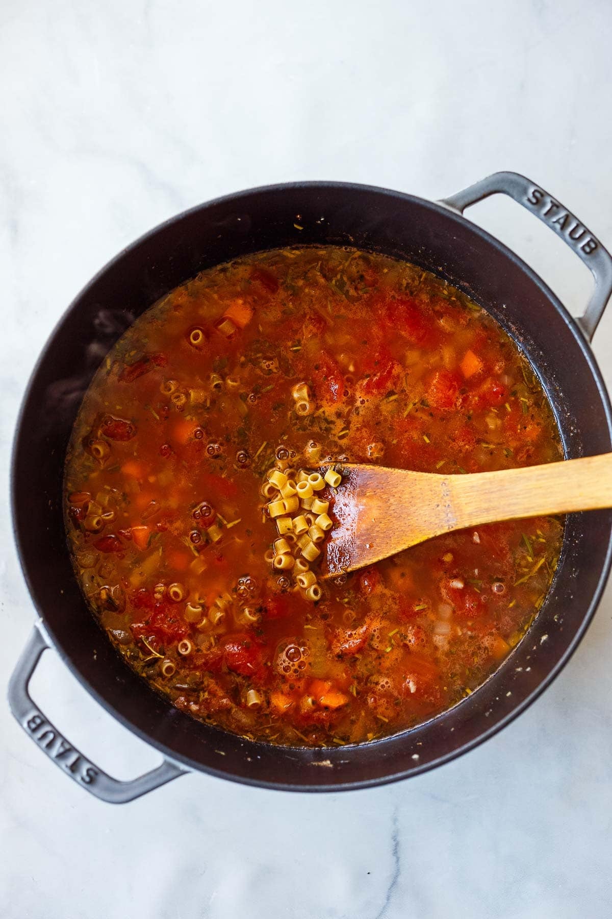making pasta e ceci with ditalini pasta, broth, dried herbs, and tomatoes in a pot. 