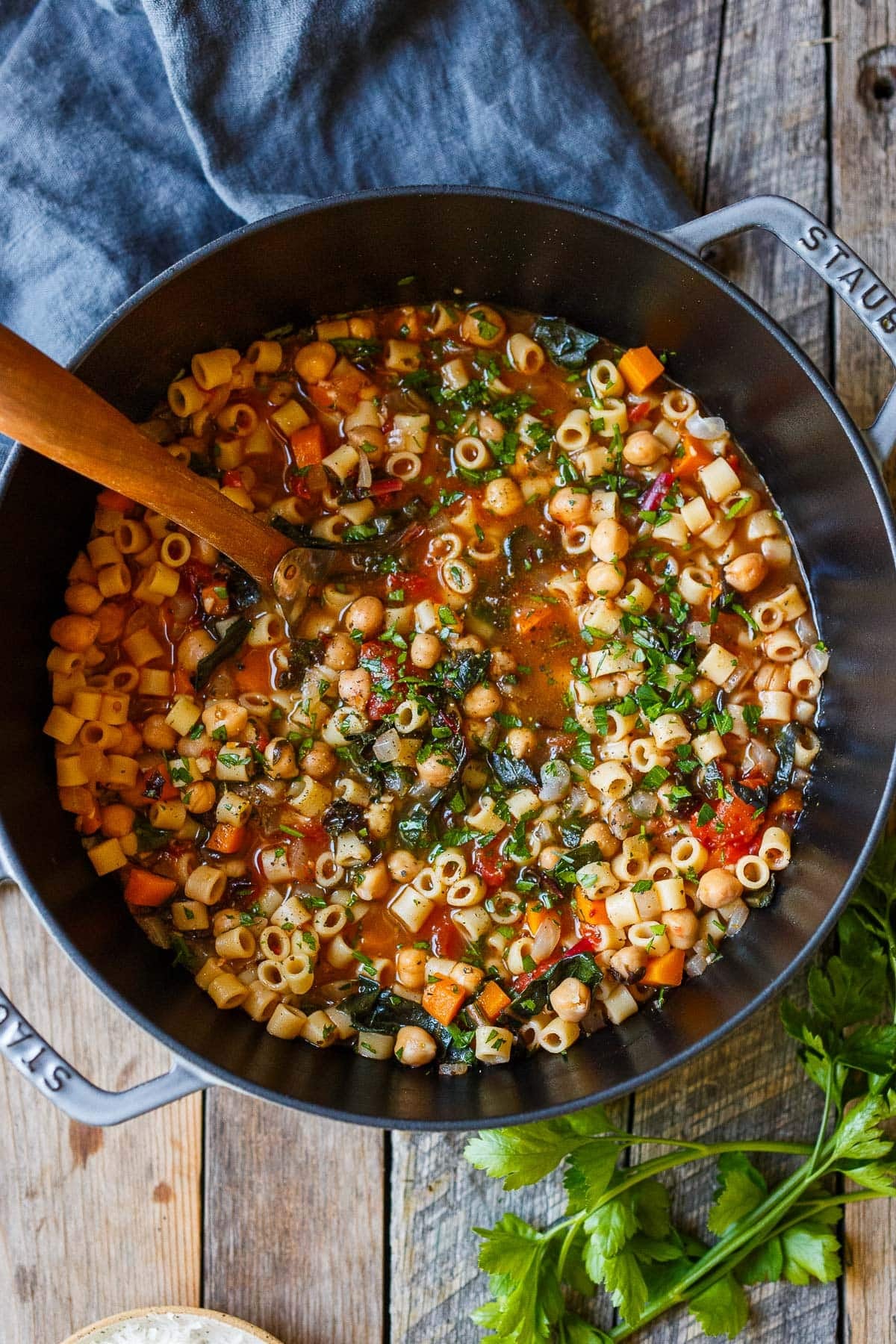 pot of pasta e ceci topped with fresh herbs, with a wooden utensil. 