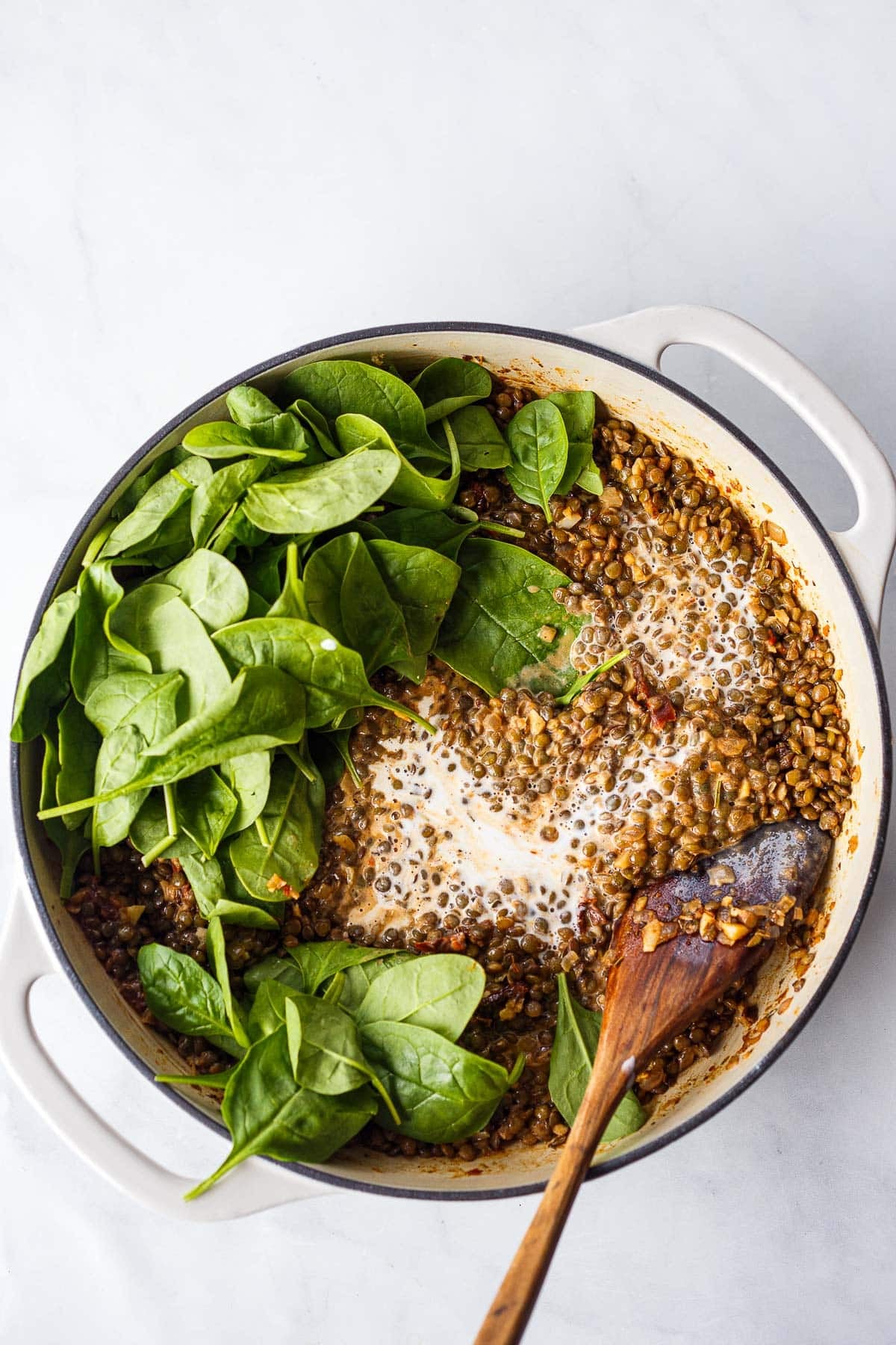 dutch oven with fresh spinach and cream added to Creamy Tuscan Lentils.