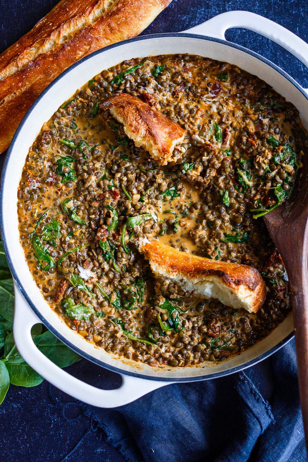 pot of Creamy Tuscan Lentils with torn crusty baguette and a wooden spoon.