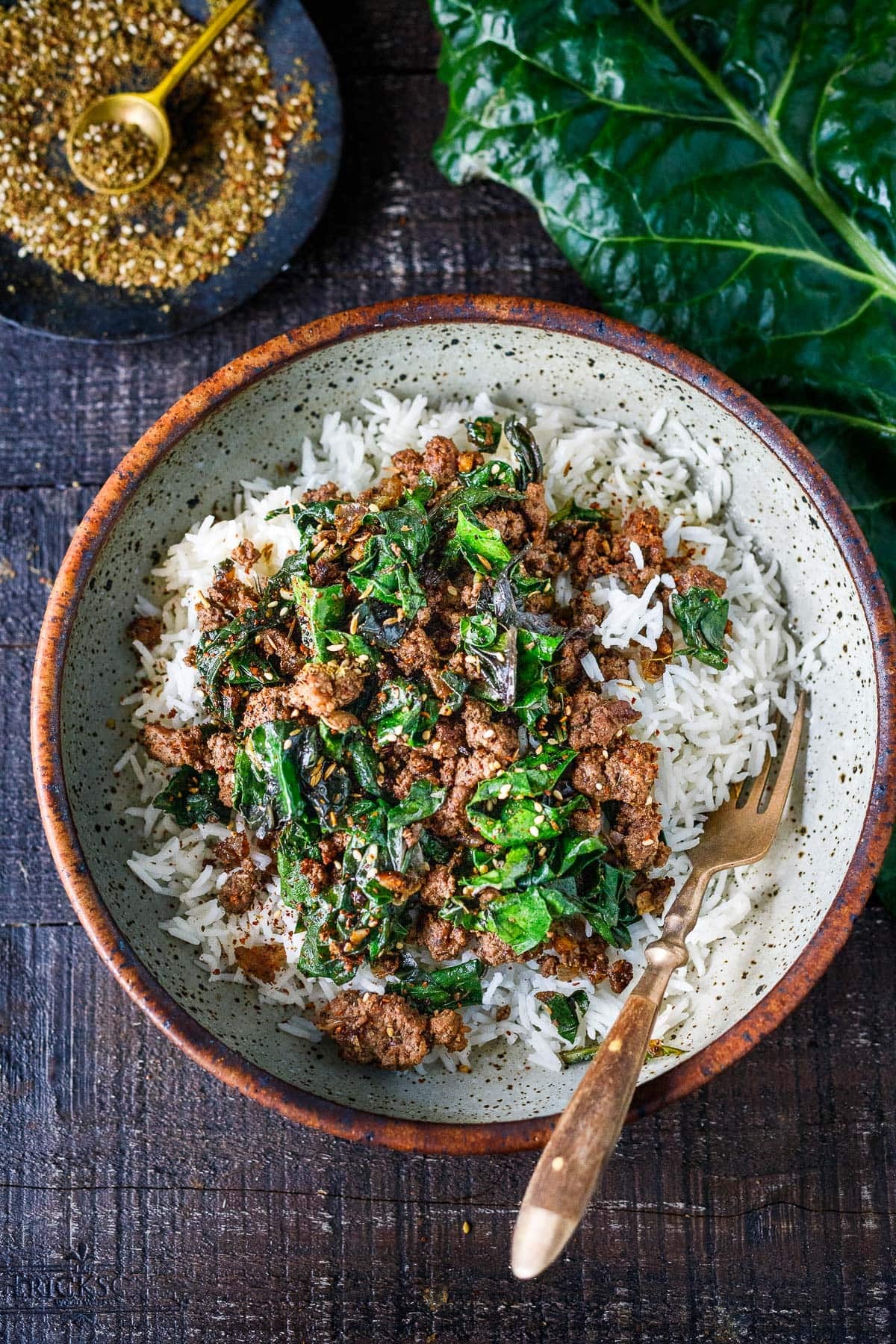 ceramic bowl with steamed basmati rice, zaatar beef and greens, and a fork.