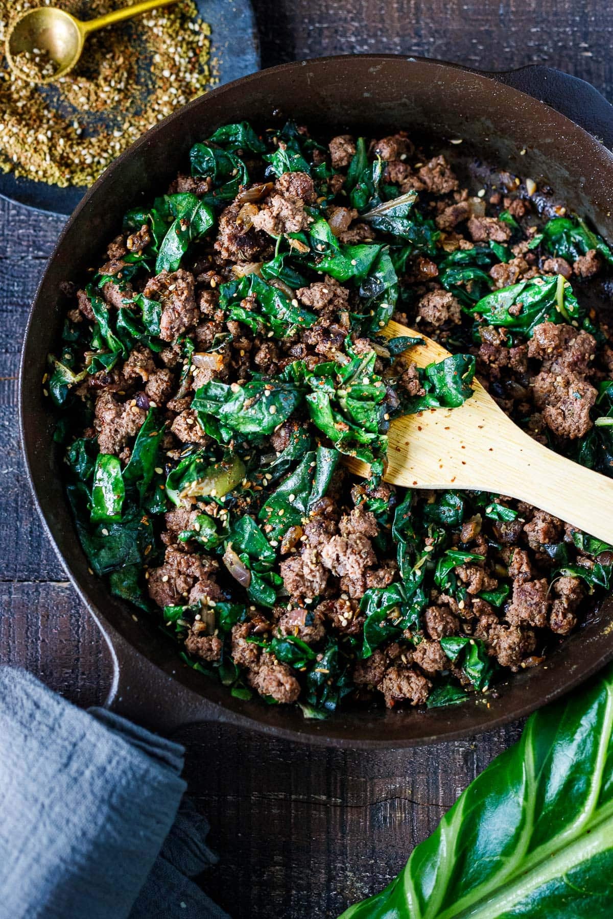 zaatar beef and greens in a cast iron skillet with a wood spatula.