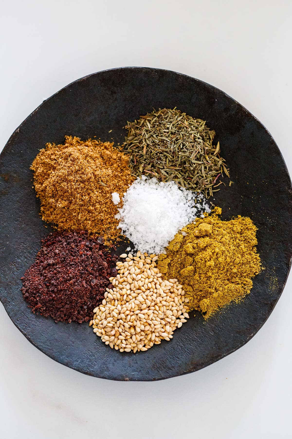 spices for making a zaatar spice blend on a black dish.