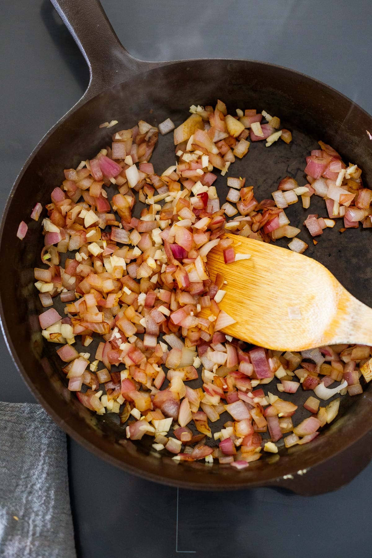 diced onion and garlic in a cast iron skillet with a wood spatula.