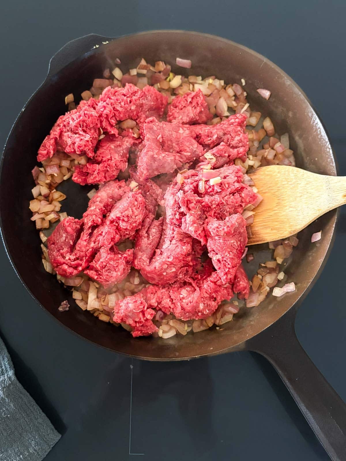 adding ground beef to a cast iron skillet with sautéed onions and garlic.